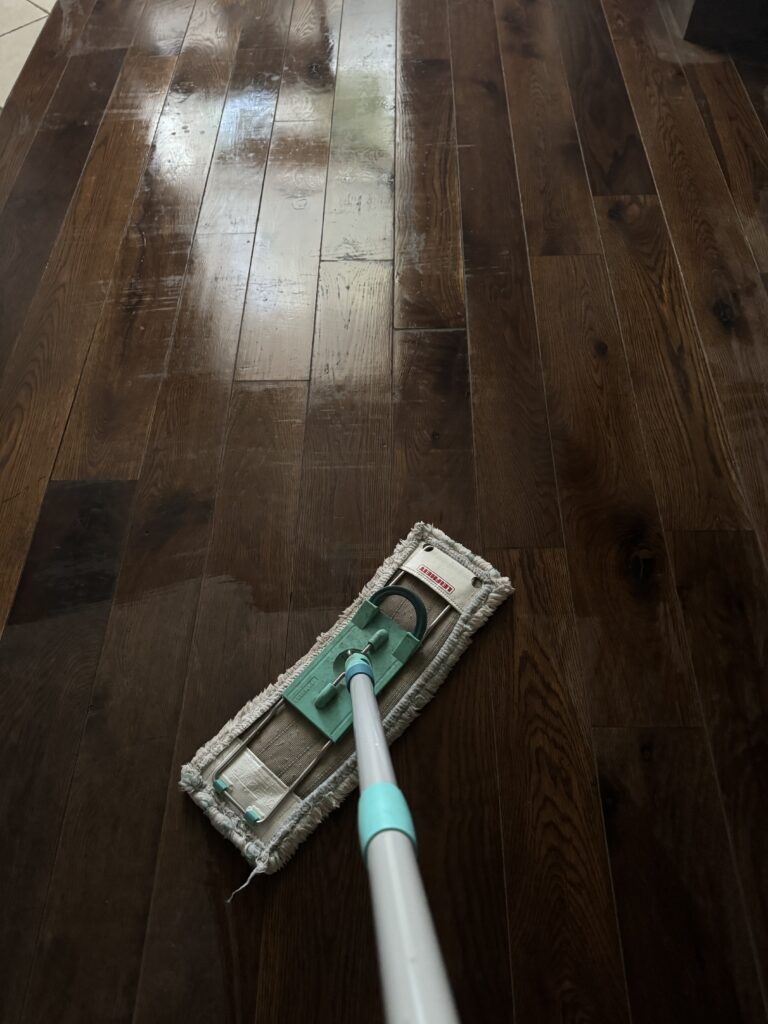 le sol en parquet en gros plan. Il brille car la serpillère vient juste d'y être passée et il est encore mouillé on voit le ballai - serpillère au premier plan