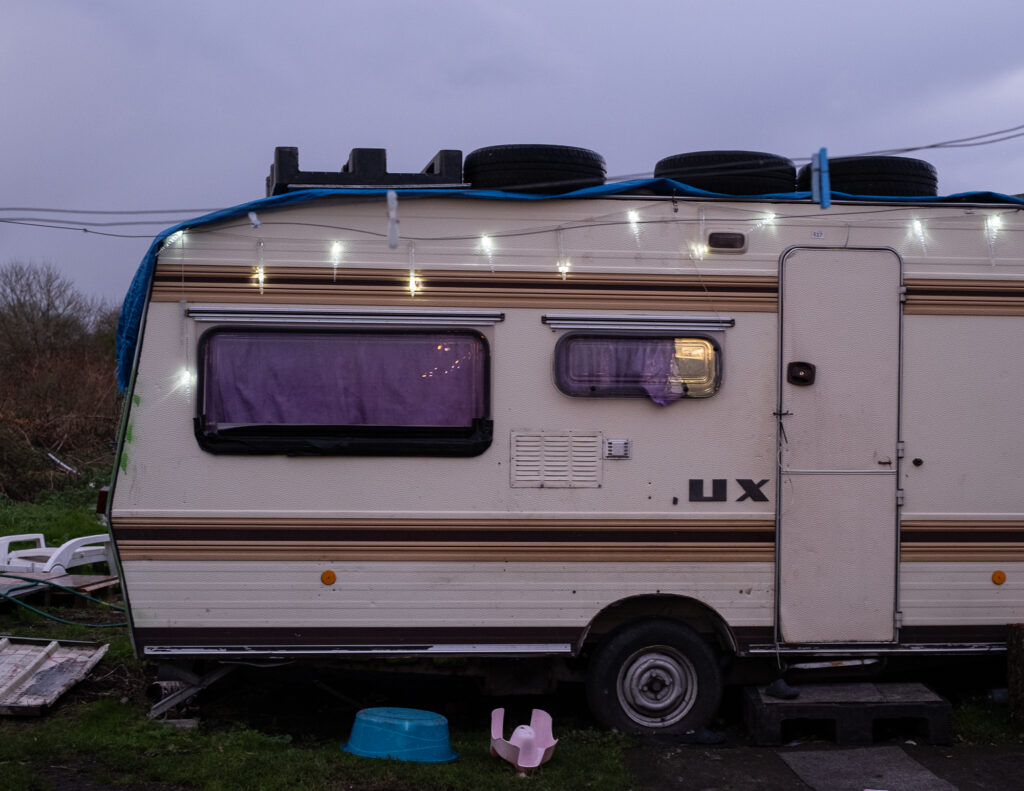 Une caravane photographiée à la nuit tombante. Une guirlande a été installée sur le haut de la caravane