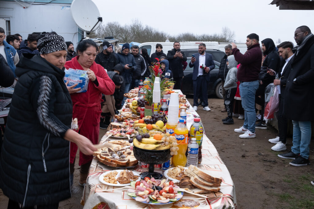 Dehors une très grande table en longueur est installée. Il y a dessus de très nombreuses victuailles et des boissons. Les bidonvilles et bidonvilloises sont réunis tout autour