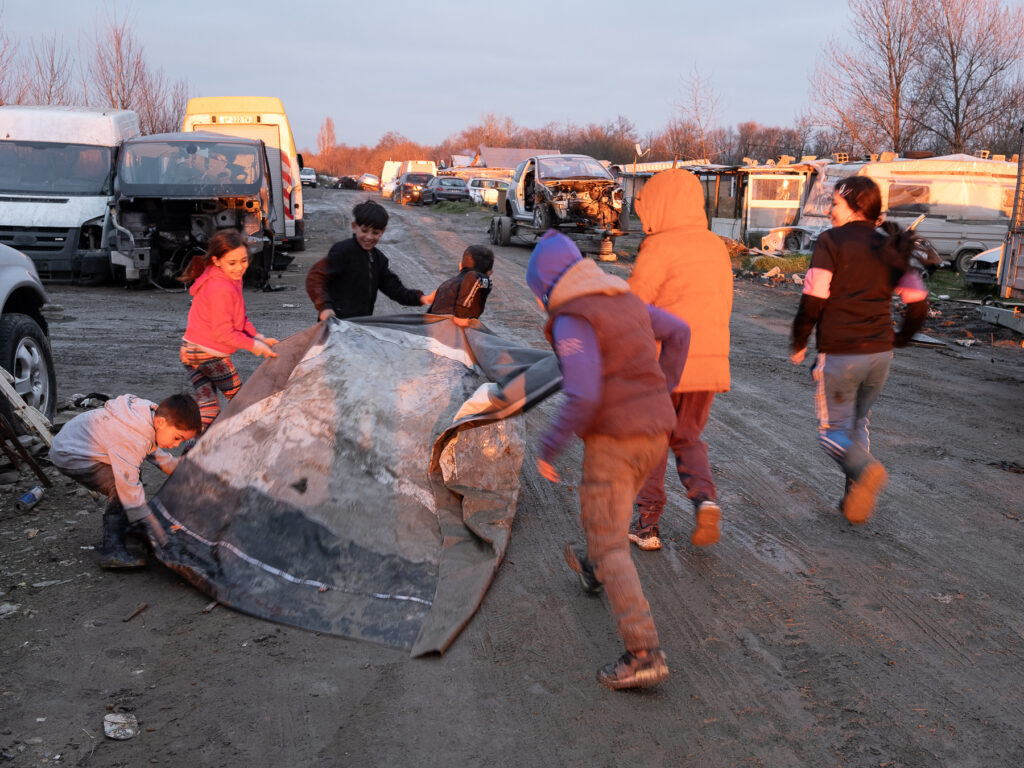 un groupe d'enfants s'amuse avec une grande bâche Sur les cotes on voit des carcasses de voiture
