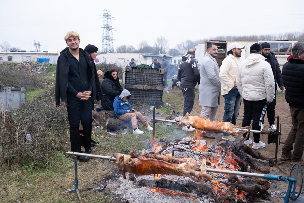 Unhomme regarde l'objectif d l'appareil photo, il se trouve près des brasero à même le sol qui permettent de cuire des porcelets.