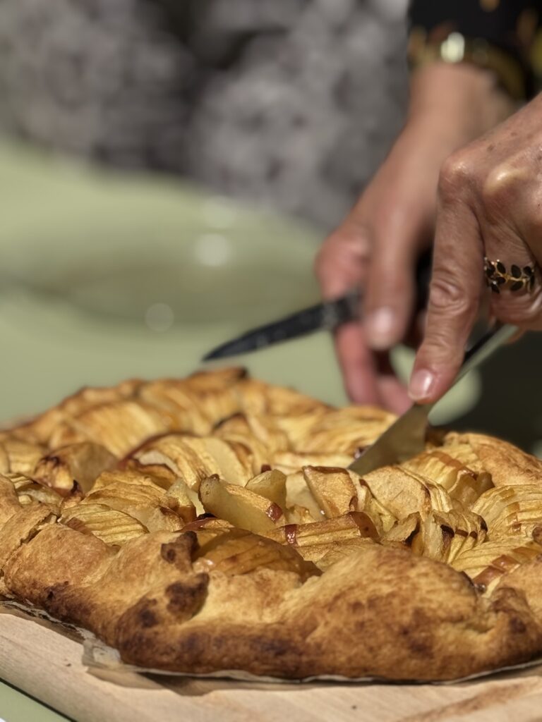 au premier plan des mains coupent une tarte aux pommes